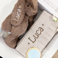 Brown plush bunny with 'Luca' embroidered on it, next to a matching blanket in a box.