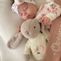 Baby sleeping with a personaliased plush bunny rabbit toy, wearing a floral outfit jumper sweater and headband. Personalised gift Australia
