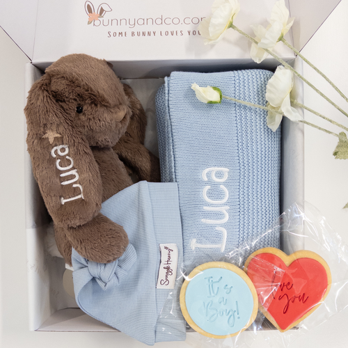 Gift set with a brown plush personalised bunny, blue baby blanket with custom name, and cookies in a box.
