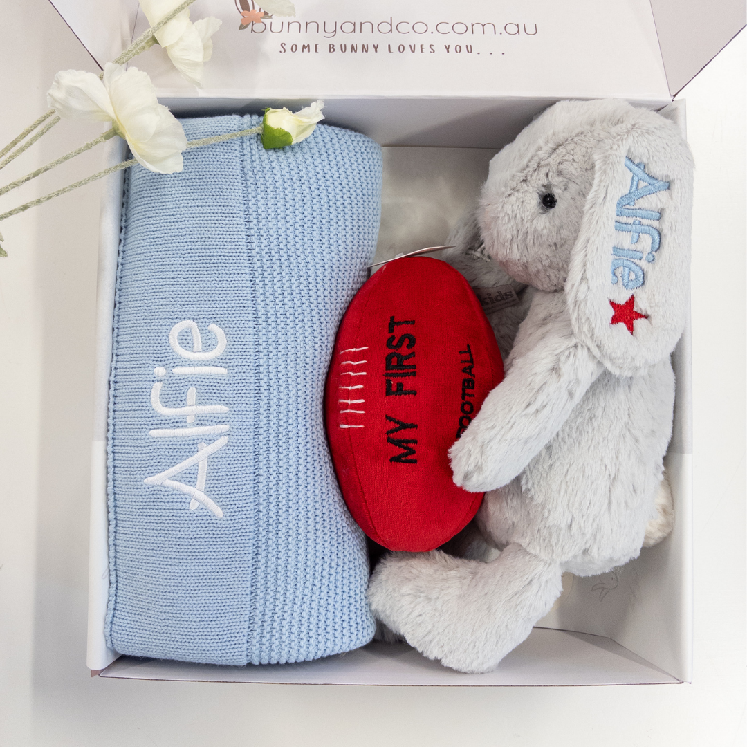 Baby gift set with blue blanket, red heart, and gray bunny toy in a box.