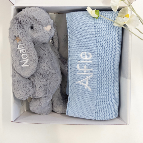 Gray plush bunny and blue knit blanket with embroidered names in a box.