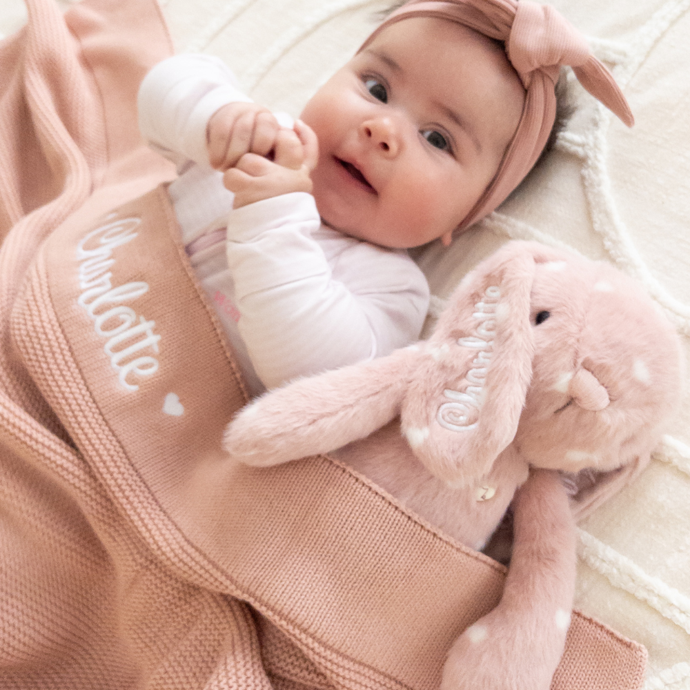 Baby lying on a pink personalised baby blanket with a plush bunny toy, engraved with name on blanket and bunny baby gift australia