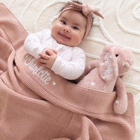 Baby lying on a pink personalised baby blanket made in Australia with a plush toy bunny, both personalised with name 'Charlotte'.