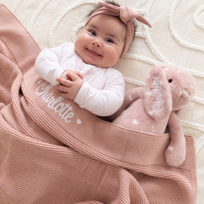 Baby lying on a pink personalised baby blanket made in Australia with a plush toy bunny, both personalised with name 'Charlotte'.