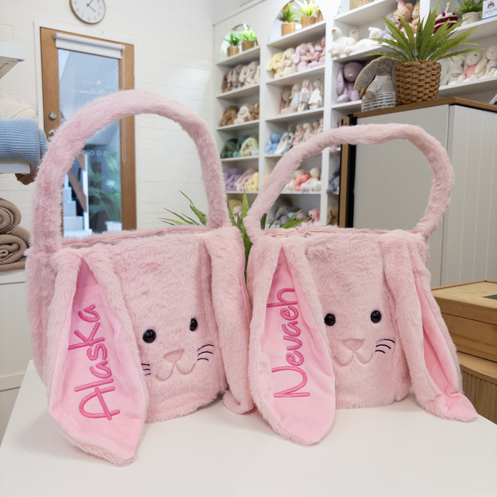 Two pink plush easter bunny bags with embroidered names on a white surface.