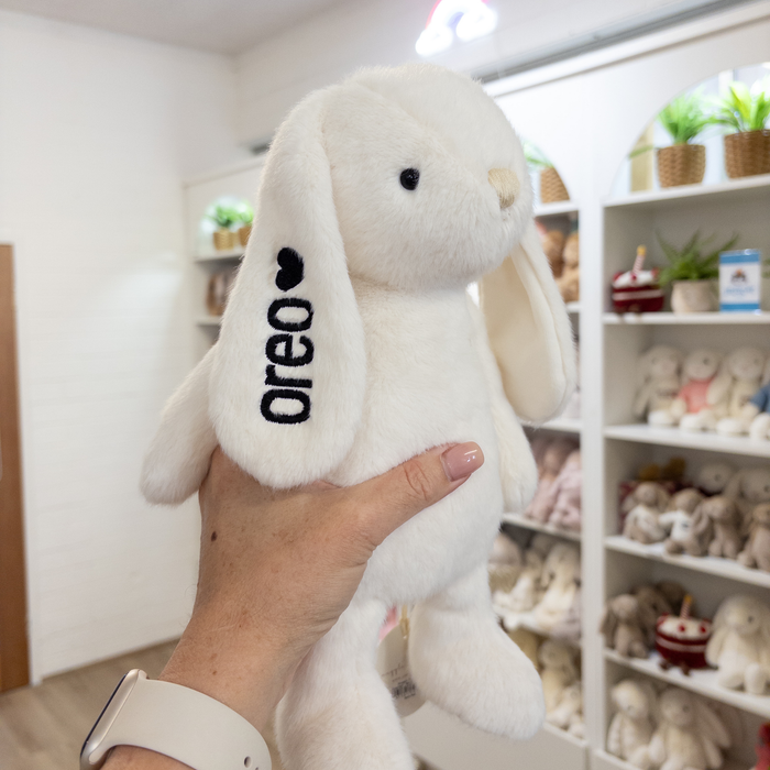 White snuggle bunnies plush toy bunny with 'oreo' branding held by a person in a store setting.